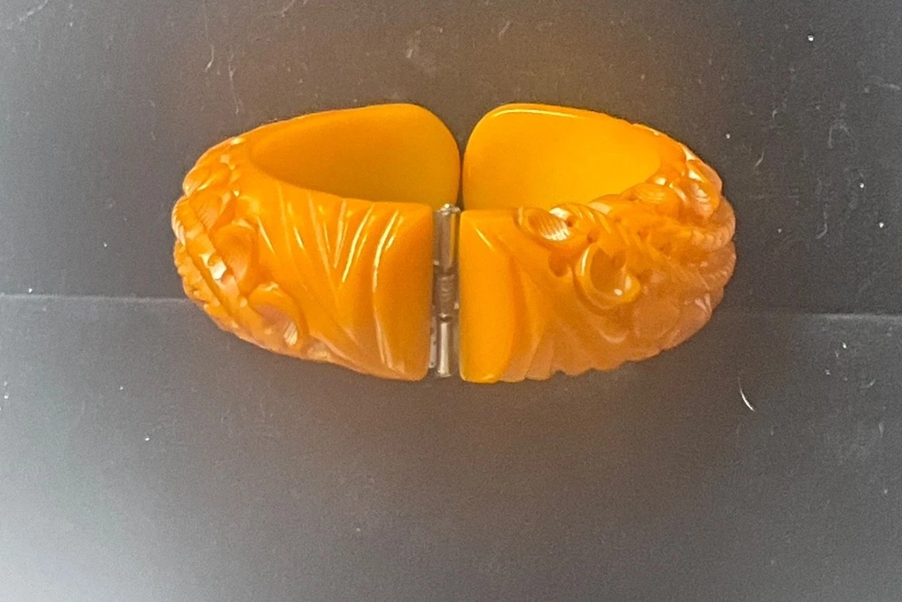 Butterscotch Bakelite clamper bracelet with deep floral carving and its metal hinge visible