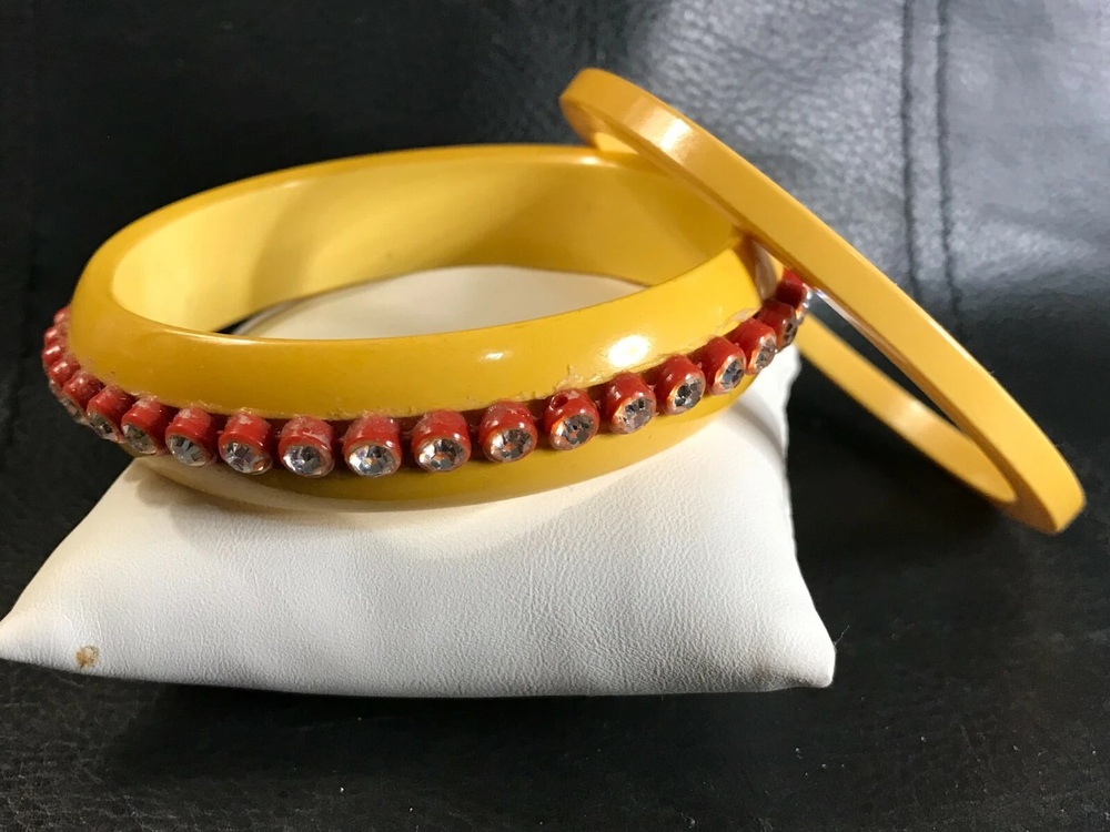 Yellow Bakelite bangle with red settings and clear rhinestones beside a narrow yellow spacer