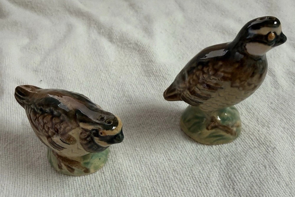 Two Rosemeade quail-shaped ceramic shakers on pale fabric.